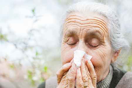 Portrait of a sick elderly woman with a napkin blowing her nose outdoorの写真素材