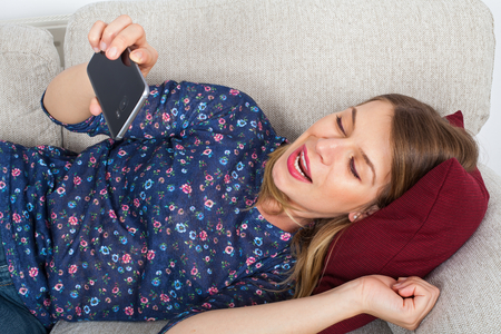 Picture of a beautiful young woman lying on the couch holding her mobile phone, having a video chatの写真素材