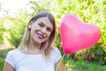 Portrait of a sexy young woman holding a heart shaped balloon posing outdoor on summertime