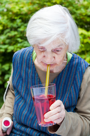 Portrait of an elderly woman with alzheimer disease drinking raspberry juice in the gardenの写真素材