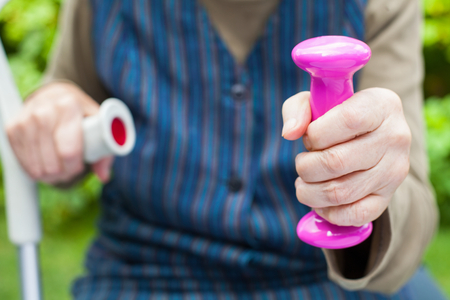 Close up picture of elderly woman's hands holding pink dumbbells outdoor on summertimeの写真素材