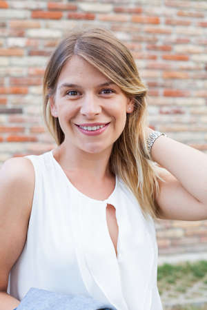 Portrait of a smiling young woman with natural look posing in front of a brick wall outdoorの写真素材