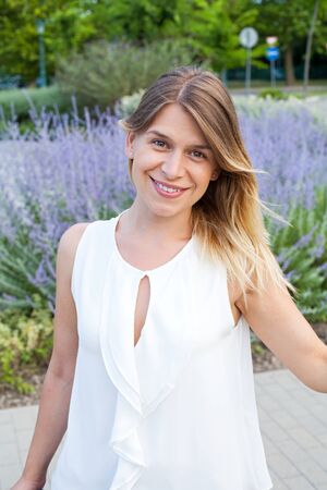 Portrait of smiling young woman posing in front of blooming lavender in the parkの写真素材