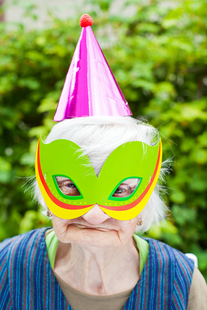 Portrait of a happy elderly woman celebrating birthday outdoor, wearing a green maskの写真素材