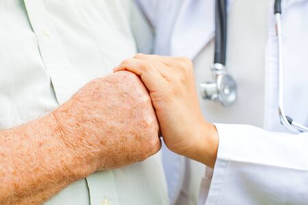Close up young female doctor holding disabled elderly man's trembling handの写真素材