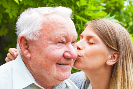 Young female giving a kiss to happy grandfather in he parkの写真素材