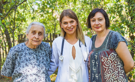 Elderly woman with her daughter and friendly young female doctor outdoorの写真素材