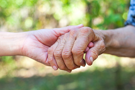 Close up elderly female's shaking hand held by young carer's hands outdoorの写真素材