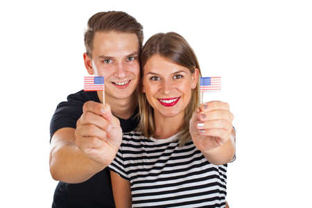 Cute young couple holding mini american flags posing on isolated background