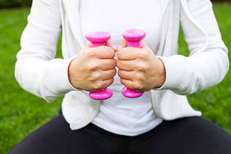 Young female doing fitness exercises with pink dumbbells in the park, green grassの写真素材
