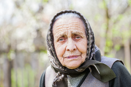 Portrait of worried old lady with headscarf looking at the camera outdoor on a sunny dayの写真素材