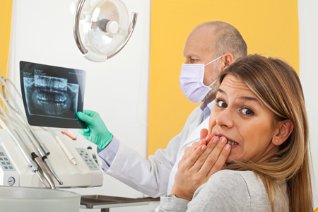 Terrified young female patient at the dentist office looking to dental x ray with doctorの写真素材