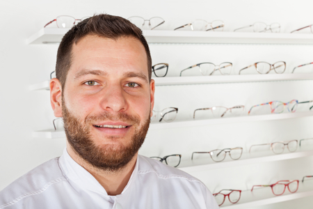 Portrait of young ophthalmologist wearing white coat, smiling at the camera in optical storeの写真素材
