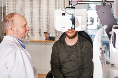 Ophthalmologist examining young man with optometric machine in optics storeの写真素材