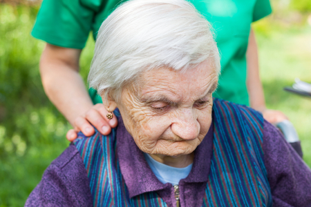 Portrait of elderly disabled woman sitting in a wheelchair spending time outdoor with friendly nurseの写真素材