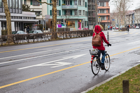 Female with red coat riding a bike on a rainy day in Bern, Switzerlandの写真素材