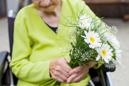Elderly paralyzed woman receiving a flower bouquet - nursing home outdoorの写真素材