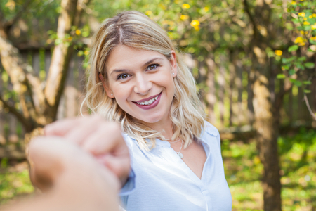 Portrait of a charming blonde woman holding her boyfriend's hand, smiling to the cameraの写真素材