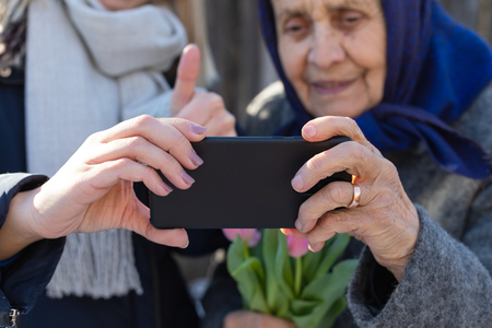 Close up picture of female hands holding a cell phone and taking a selfie - old woman portraitの写真素材