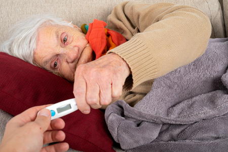 Close up picture senior woman being sick, carer holding digital thermometer next to her head - feverの写真素材