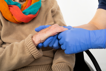 Close up picture of medical nurse wearing blue sterile gloves holding old disabled woman's handsの写真素材