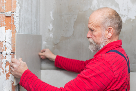 Picture of an elderly craftsman putting tiles on the wall in the bathroom at a new apartmentの写真素材