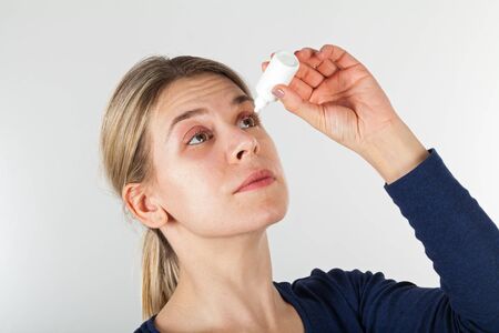 Portrait of a young woman with severe eye infection using medical teardrops - isolated background