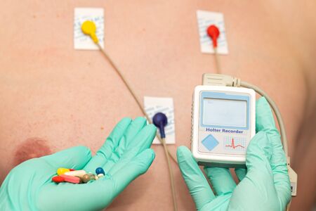 Doctor's hand applying holter heart monitor on young man's chest