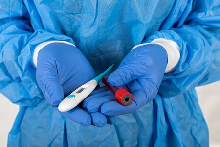 Close up medical surgeon holding digital thermometer and blood sample. COVID-19 test results