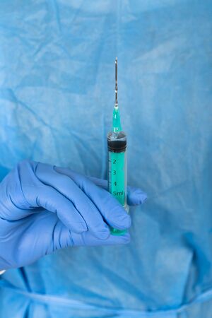 Close up picture of medical surgeon with protective uniform and gloves holding a syringeの写真素材