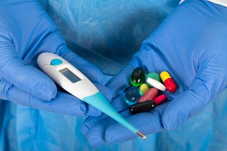 Close up picture of surgeon holding digital thermometer and medical drugs on blue backgroundの写真素材
