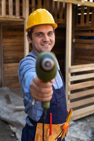 Portrait of a handsome young craftsman with yellow hard hat holding an electric drill