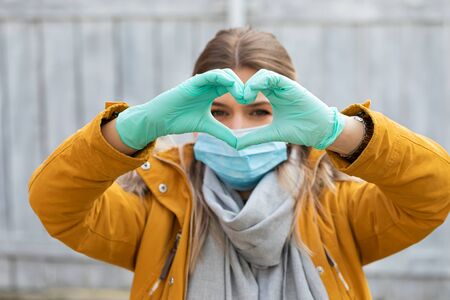 Young woman with protective mask and gloves showing heart symbol - covid-19 pandemic alertの写真素材
