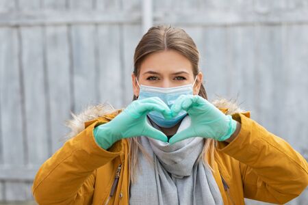 Woman with surgical mask and gloves showing heart symbol. Coronavirus pandemic. Stay safeの写真素材