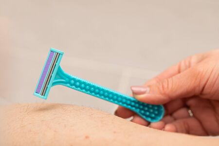 Close up picture of woman holding razor, shaving her hairy leg with folliculitisの写真素材