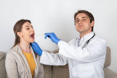 Young male doctor consulting female patient with influenza symptoms at homeの写真素材