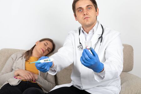 Young male doctor consulting female patient with influenza symptoms at homeの写真素材