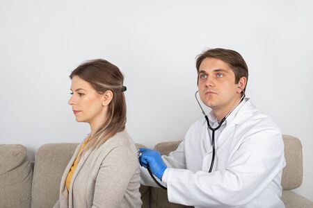 Young male doctor consulting female patient with influenza symptoms at homeの写真素材