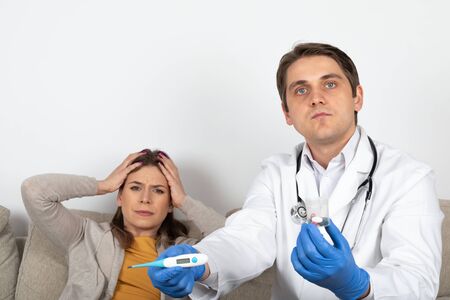 Young male doctor consulting female patient with influenza symptoms at homeの写真素材