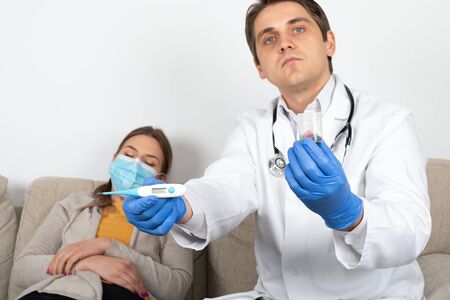 Young male doctor consulting female patient with influenza symptoms at homeの写真素材