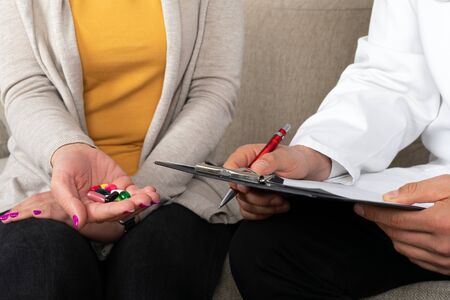 Close up picture of doctor giving medication and supplements to female patient, both seated on the couchの写真素材