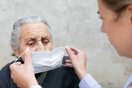 Nurse putting on surgical mask on elderly ill woman - coronavirus protective protocolの写真素材