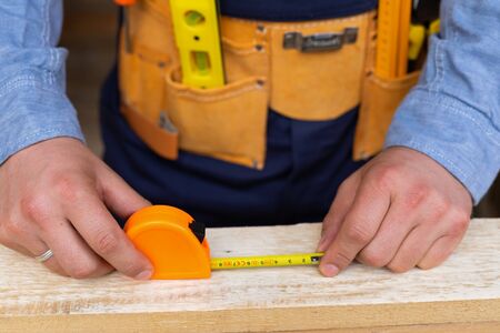 Close up picture of carpenters hands measuring plank - DIY renovation at home