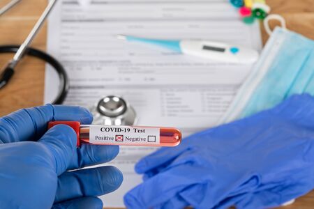 Close up picture of positive covid-19 blood test and medical supplies, treatment, mask and gloves on...