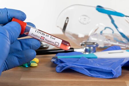 Close up picture of positive covid-19 blood test and medical supplies, treatment, mask and gloves on...