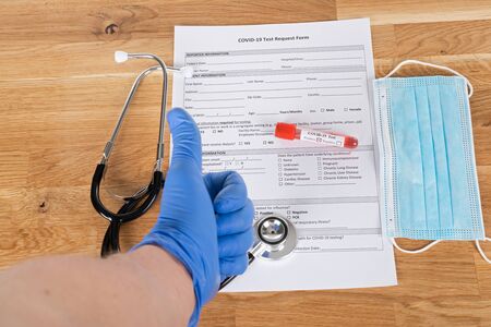 Close up picture of positive covid-19 blood test and medical supplies, treatment, mask and gloves on wooden backgroundの写真素材