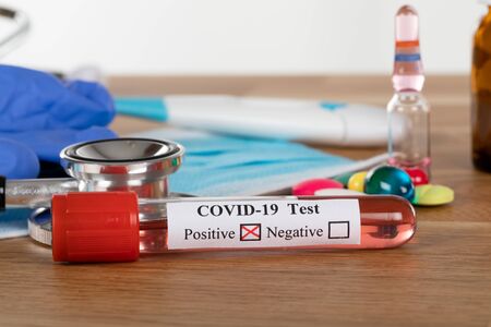 Close up picture of positive covid-19 blood test and medical supplies, treatment, mask and gloves on wooden backgroundの写真素材