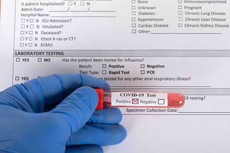 Doctors hand wearing protective glove holding Covid-19 blood test in front of patients form