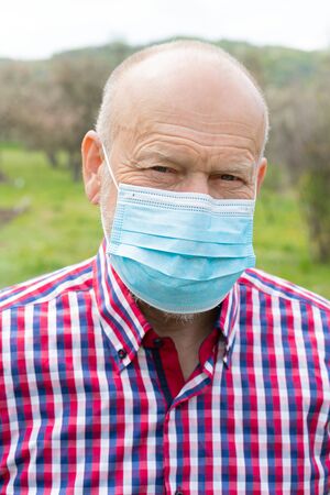 Portrait of elderly man with surgical mask spending time outdoors in the gardenの写真素材