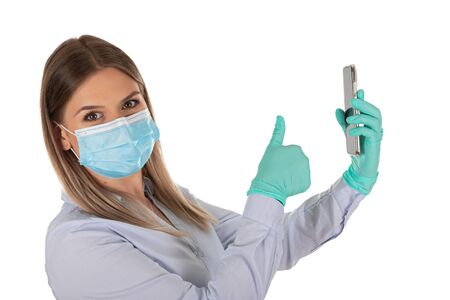 Beautiful caucasian woman with mask and gloves having a video call on isolated backgroundの写真素材